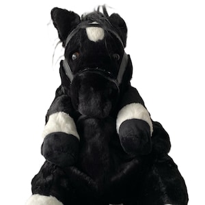 May include: Black and white plush horse backpack with a black leather bridle. The horse has a white star on its forehead.