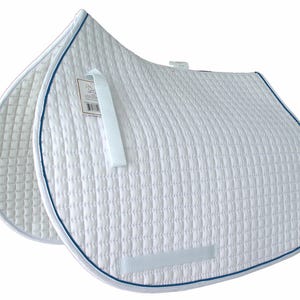 Pode incluir: Almofada de sela acolchoada branca com acabamento azul marinho. A almofada tem formato retangular com bordas arredondadas e uma alça branca. Uma etiqueta está presa na parte superior da almofada. A almofada é projetada para uso equestre.