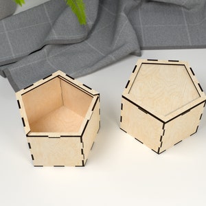 May include: Two hexagonal wooden boxes with lids. The boxes are made of light wood with a natural finish. The lids are closed and the boxes are sitting on a white surface.