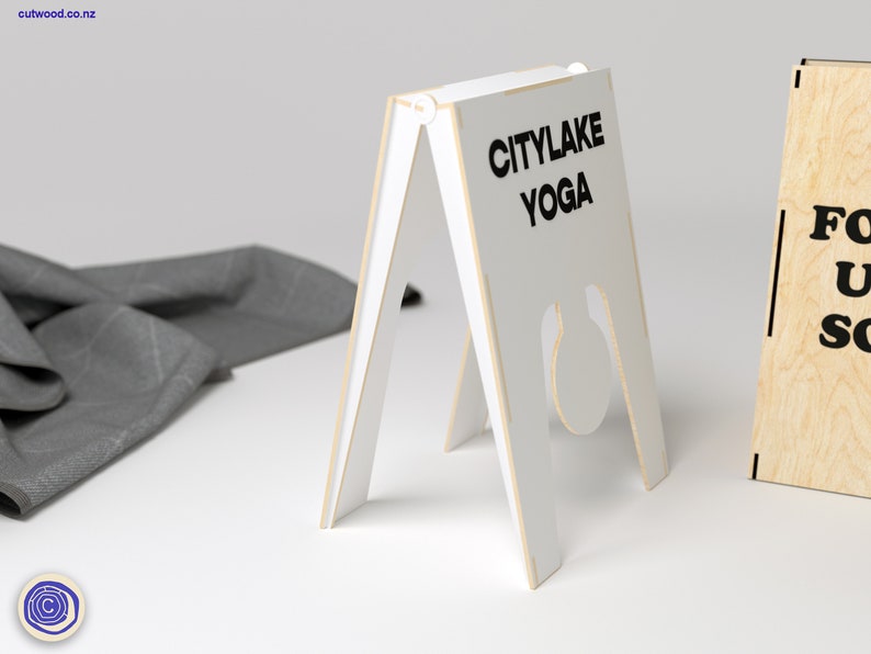 May include: White wooden A-frame sign with the text "CITYLAKE YOGA" in black lettering. The sign is standing on a white surface.