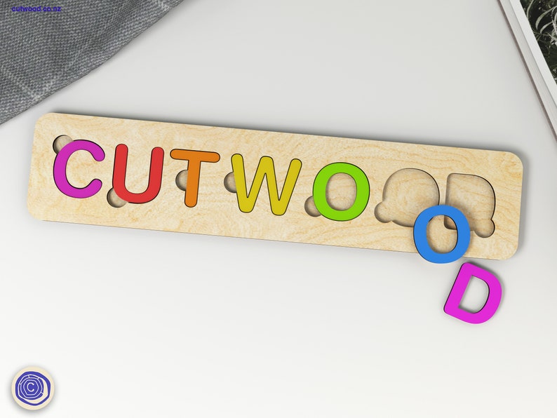 Puede incluir: Un rompecabezas de madera con la palabra "CUTWOOD" escrita en letras de colores. Las letras faltan en sus ranuras y est&aacute;n dispersas alrededor del rompecabezas.
