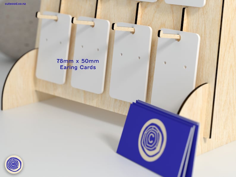 May include: A wooden display stand with white earring cards. The cards are 78mm x 50mm and have two holes for displaying earrings. The stand has a blue business card with a logo on it.