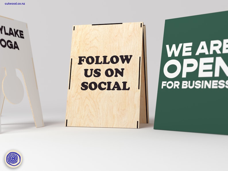 May include: Three wooden A-frame signs. The sign on the left is white with the text "AYLAKE YOGA". The middle sign is made of wood with the text "FOLLOW US ON SOCIAL". The sign on the right is green with the text "WE ARE OPEN FOR BUSINESS".