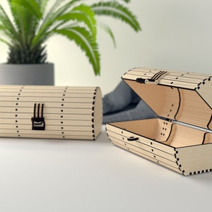 Op de afbeelding: Twee houten dozen met een cilindrische vorm en een scharnierend deksel. De dozen hebben een zwart slot en zijn versierd met zwarte lijnen en stippen.