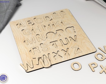 May include: Wooden alphabet puzzle with uppercase letters cut out of a light brown board. The letters are scattered around the board, with some letters missing.