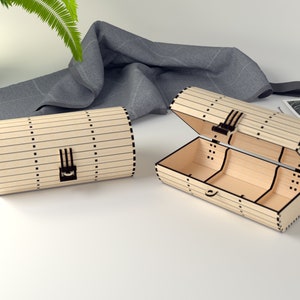 Op de afbeelding: Twee houten dozen met een scharnierend deksel en een sluiting. De dozen zijn gemaakt van licht hout met zwarte lijnen en stippen. De doos rechts is open en laat een compartiment met drie secties zien.