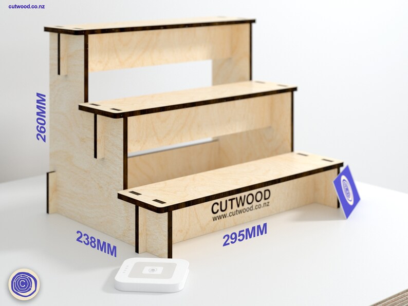 May include: A three-tiered wooden display stand made of plywood. The stand is 260mm tall, 238mm wide, and 295mm deep. The stand is made of natural wood with a light brown color. The stand has a simple design with three shelves and a small logo on the bottom shelf that reads "CUTWOOD www.cutwood.co.nz".