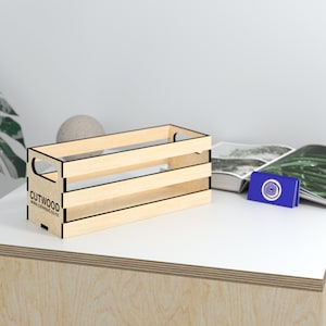 Op de afbeelding: Een natuurlijke houten kist met een zwarte omtrek en de tekst "CUTWOOD www.cutwood.co.nz" aan de voorkant. De kist staat op een licht houten oppervlak.