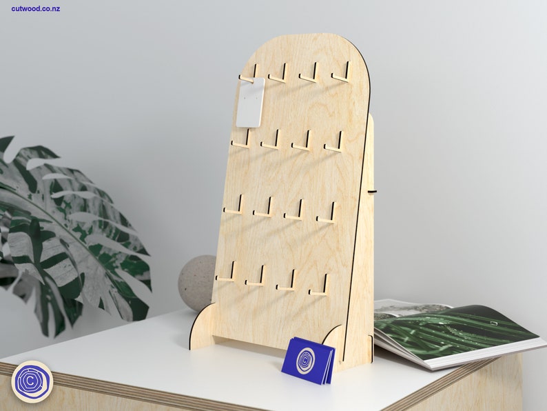 May include: A wooden display stand with a rounded top and multiple hooks for hanging earrings or other small items. The stand is made of light-coloured wood and has a natural finish. It is standing on a white surface.