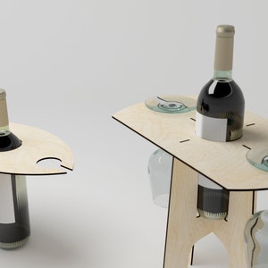 May include: Wooden wine table with a bottle of red wine, two wine glasses, and a small plate. The table has a unique design with a cutout for the wine bottle and a slot for the wine glass.