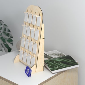 May include: A wooden display stand with 16 white rectangular slots for holding small items. The stand is made of light wood and has a rounded top. The stand is on a light wood surface.