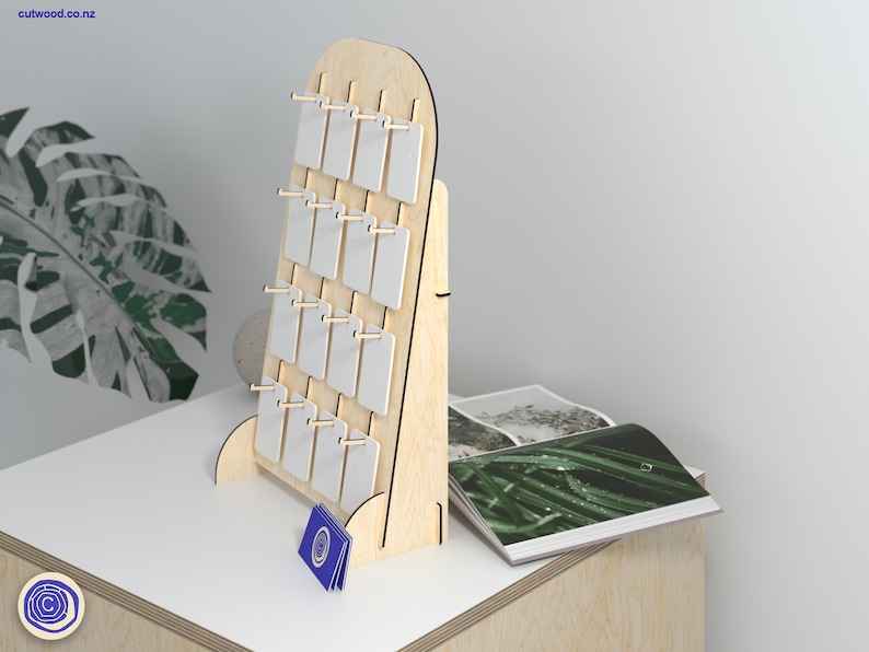 May include: A wooden display stand with 16 white rectangular slots for holding small items. The stand is made of light wood and has a rounded top. The stand is on a light wood surface.