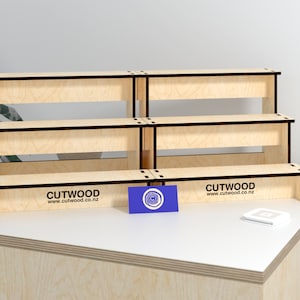 May include: Three tiered wooden display stand with a natural wood finish and black trim. The stand is made of plywood and has the text "CUTWOOD www.cutwood.co.nz" printed on the bottom tier.