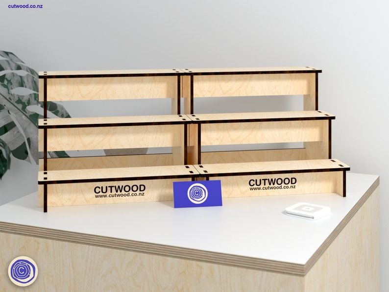May include: Three tiered wooden display stand with a natural wood finish and black trim. The stand is made of plywood and has the text "CUTWOOD www.cutwood.co.nz" printed on the bottom tier.