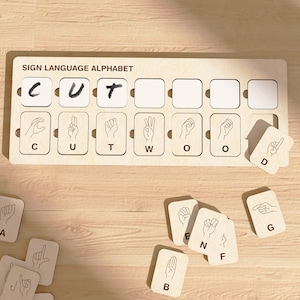 May include: A wooden board with the words "SIGN LANGUAGE ALPHABET" printed on it. The board has eight slots, each with a letter of the alphabet in sign language. The letters are C, U, T, W, O, O, D. There are also several individual wooden tiles with letters of the alphabet in sign language.