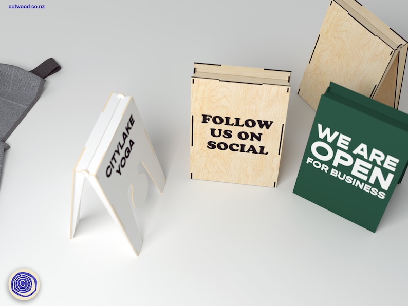 May include: Three wooden A-frame signs with different messages. The first sign is white with black text that reads "Citylake Yoga". The second sign is light brown with black text that reads "Follow us on Social". The third sign is green with white text that reads "We are Open for Business".