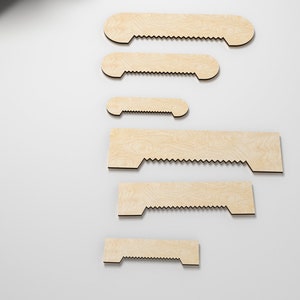 Puede incluir: Seis soportes de estantería de madera de diferentes tamaños, todos de color marrón claro y con un borde festoneado.