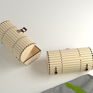 Op de afbeelding: Twee houten dozen met een cilindrische vorm en een scharnierend deksel. De dozen zijn gemaakt van lichtbruin hout met zwarte lijnen en stippen. De doos aan de linkerkant is open, waardoor de binnenkant van de doos zichtbaar is. De doos aan de rechterkant is gesloten.