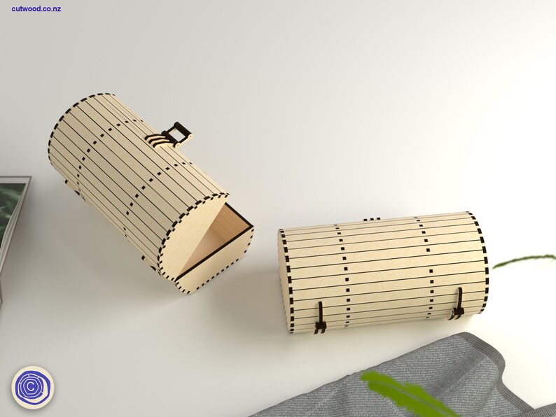 Op de afbeelding: Twee houten dozen met een cilindrische vorm en een scharnierend deksel. De dozen zijn gemaakt van lichtbruin hout met zwarte lijnen en stippen. De doos aan de linkerkant is open, waardoor de binnenkant van de doos zichtbaar is. De doos aan de rechterkant is gesloten.