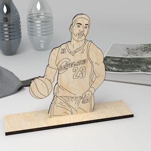 May include: A wooden cutout of a basketball player wearing a jersey with the text "Cleveland 23". The player is holding a basketball and is standing on a wooden base.