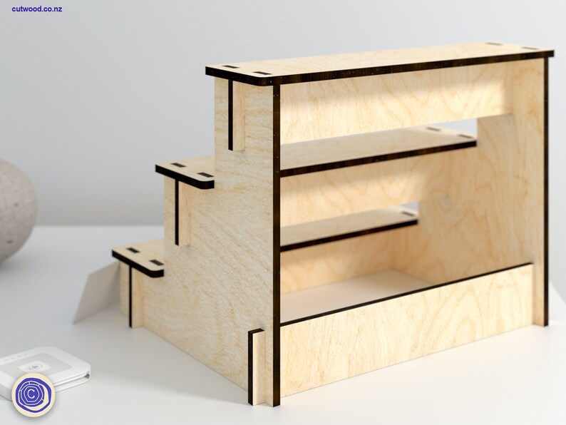 May include: A wooden tiered shelf unit with three shelves and a base. The shelf unit is made of light wood with black edges and is designed to display small items.