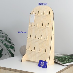 May include: A wooden display stand with hooks for hanging earrings or other small items. The stand is 69 cm tall and 49 cm wide. It has a light wood finish and is made of plywood.