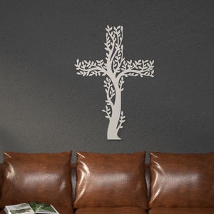 Peut inclure: Une croix murale en forme d'arbre de couleur claire. La croix est faite d'un matériau clair et présente un motif d'arbre avec des feuilles. La croix est fixée sur un mur gris foncé au-dessus d'un canapé en cuir marron.