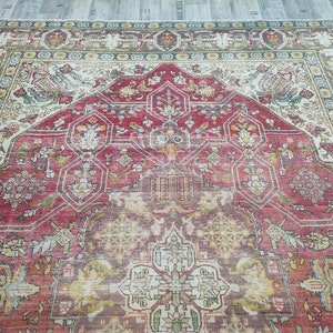 May include: A vintage Persian rug with a red, cream, and green color scheme. The rug features a central medallion with intricate floral and geometric patterns. The rug has a worn and faded appearance, adding to its antique charm.