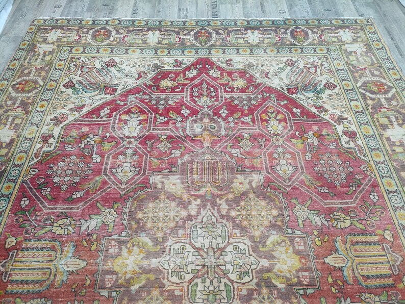 May include: A vintage Persian rug with a red, cream, and green color scheme. The rug features a central medallion with intricate floral and geometric patterns. The rug has a worn and faded appearance, adding to its antique charm.