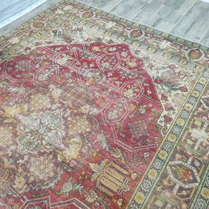 May include: A vintage rug with a red, cream, and green floral pattern. The rug has a central medallion with a geometric design and a border with a repeating pattern.
