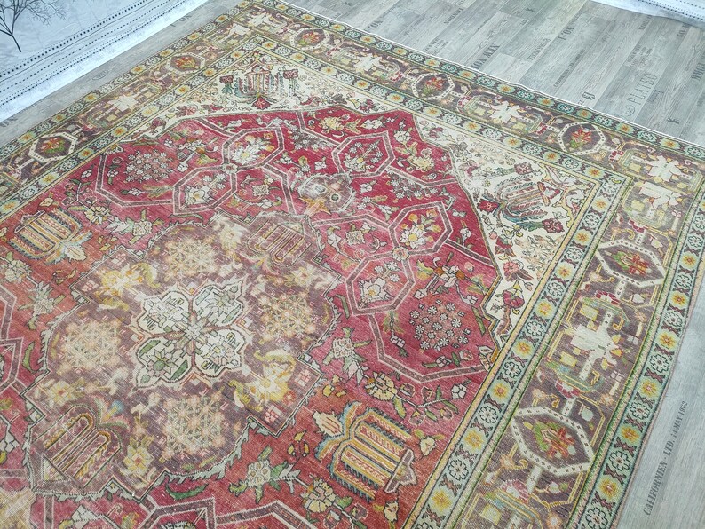 May include: A vintage rug with a red, cream, and green floral pattern. The rug has a central medallion with a geometric design and a border with a repeating pattern.