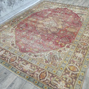 May include: A vintage rug with a cream background and a large, intricate, red and brown floral pattern in the center. The rug has a faded, distressed look, giving it a unique and antique feel.