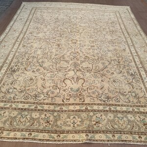 May include: A large, cream-coloured rug with a floral pattern in shades of brown and beige. The rug has a border with a repeating pattern of brown, beige, and green.
