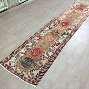 May include: A long, narrow rug with a traditional Turkish design. The rug has a cream background with red, pink, orange, and blue geometric patterns.