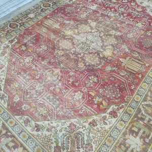 May include: A vintage rug with a faded red center and intricate floral patterns. The rug has a cream-colored border with a geometric design.