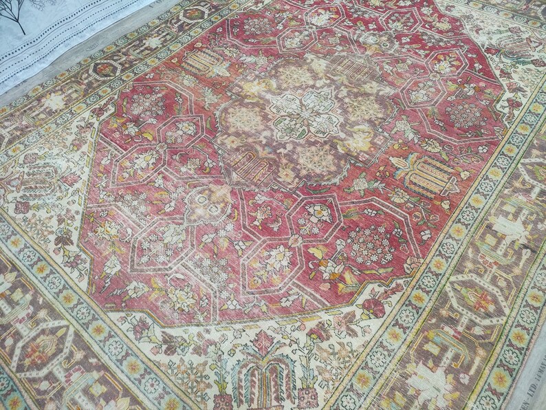 May include: A vintage rug with a faded red center and intricate floral patterns. The rug has a cream-colored border with a geometric design.