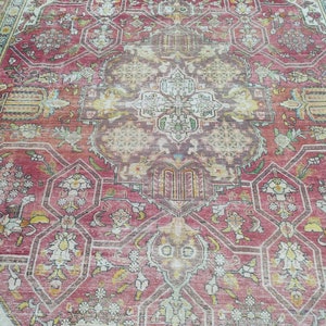 May include: A vintage rug with a faded red background and intricate floral patterns in shades of cream, yellow, and green. The rug has a central medallion with a geometric design.