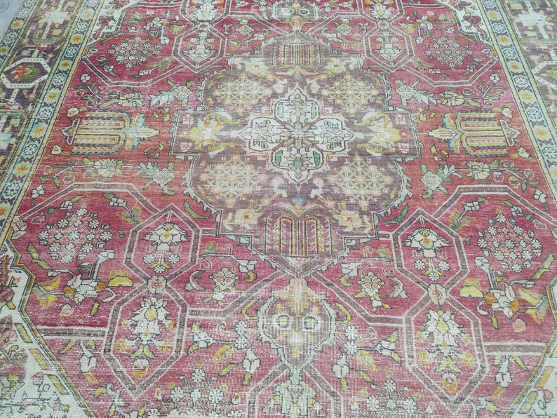 May include: A vintage rug with a faded red background and intricate floral patterns in shades of cream, yellow, and green. The rug has a central medallion with a geometric design.