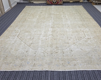 May include: A large rectangular area rug featuring a faded beige and cream color palette with intricate, low-contrast floral and geometric patterns throughout the field and a detailed border with subtle blue and grey accents.
