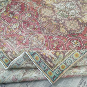 May include: A vintage rug with a faded red, cream, and blue floral pattern. The rug is folded in half, showing the back side, which is a lighter cream color.