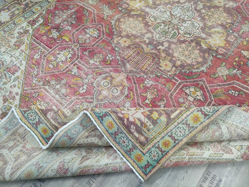 May include: A vintage rug with a faded red, cream, and blue floral pattern. The rug is folded in half, showing the back side, which is a lighter cream color.