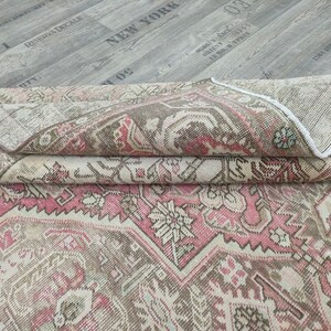 May include: A folded vintage rug with a pink and beige geometric pattern. The rug has a fringed edge and is made of wool.