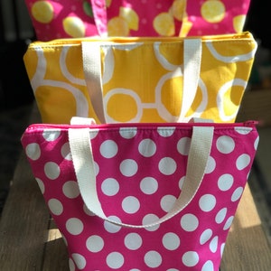 Peut inclure: Trois sacs isothermes r&eacute;utilisables avec fermeture &eacute;clair et poign&eacute;es blanches. Le sac du haut a un fond rose avec des citrons et des feuilles vertes. Le sac du milieu a un fond jaune avec des cercles blancs. Le sac du bas a un fond rose avec des pois blancs.