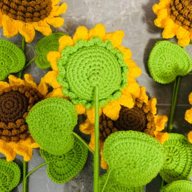 May include: A set of crocheted sunflowers with green leaves. The sunflowers are yellow with brown centers and the leaves are a bright green.