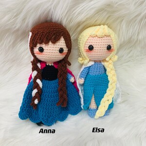 Peut inclure: Deux poup&eacute;es en crochet, l'une avec des cheveux bruns et une robe bleue, l'autre avec des cheveux blonds et une robe bleu clair. La poup&eacute;e aux cheveux bruns est &eacute;tiquet&eacute;e "Anna" et la poup&eacute;e aux cheveux blonds est &eacute;tiquet&eacute;e "Elsa".