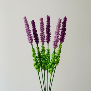 May include: A bouquet of crocheted lavender flowers in shades of purple and green. The flowers are arranged in a bunch and have a realistic appearance.