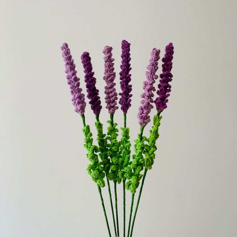 May include: A bouquet of crocheted lavender flowers in shades of purple and green. The flowers are arranged in a bunch and have a realistic appearance.