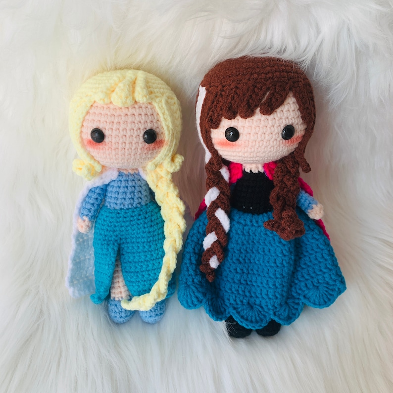 Puede incluir: Dos mu&ntilde;ecas de crochet, una con cabello rubio y un vestido azul, la otra con cabello casta&ntilde;o y un vestido azul y rosa.