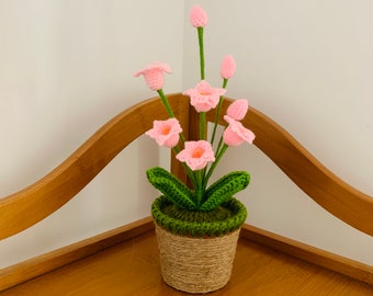 May include: A crocheted pink flower arrangement in a brown pot with green leaves. The pot is wrapped in twine.