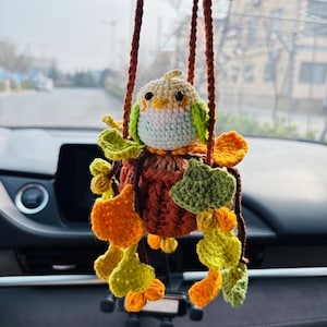 Peut inclure: Un charm de voiture en forme d'oiseau crocheté. La tête est crème avec des touches de vert, la poitrine bleu clair. Le corps est marron et orange, avec des ornements en forme de feuilles vertes et oranges. Suspendu par des cordons bruns.